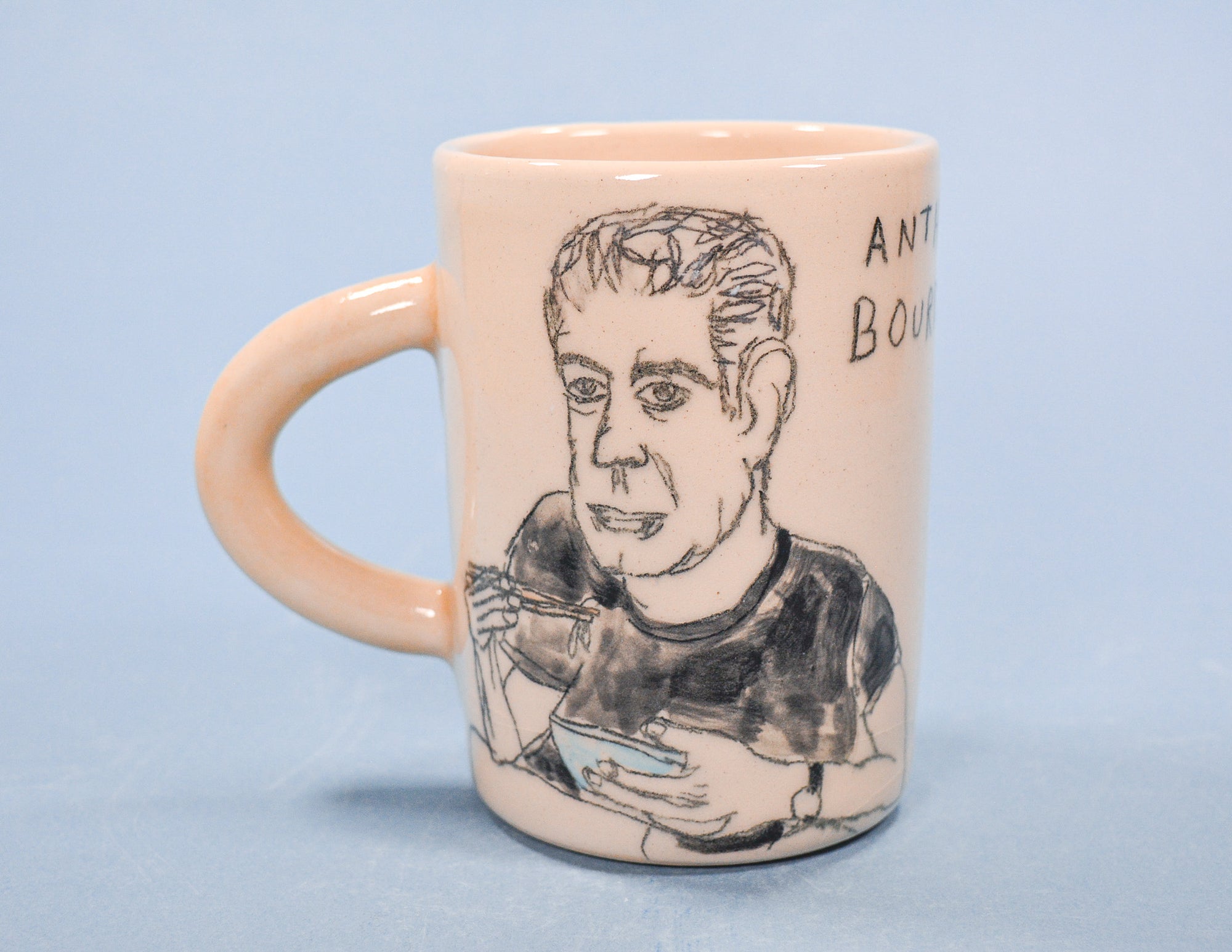 Mug with a portrait illustration of Anthony Bourdain and text on a light blue background