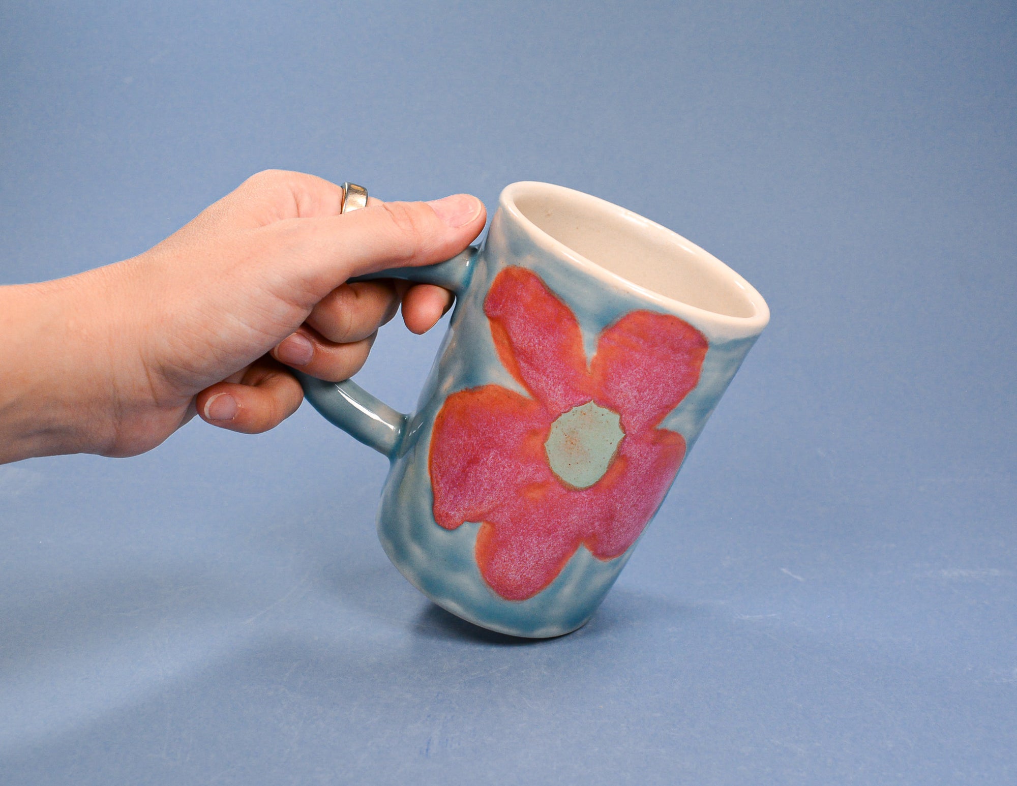 Hand holding a mug with a pink flower design against a blue background