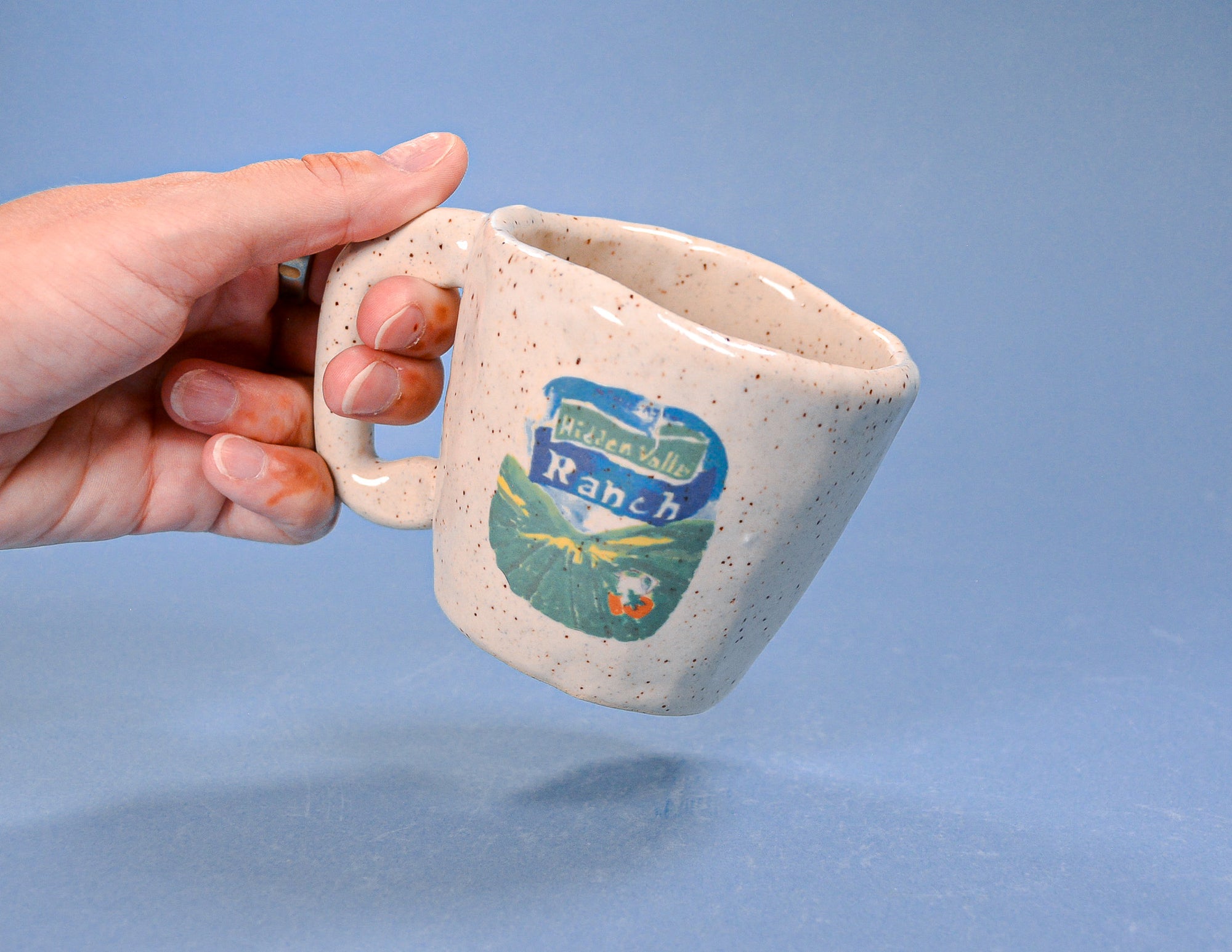 Hand holding a ceramic mug with a logo on a blue background