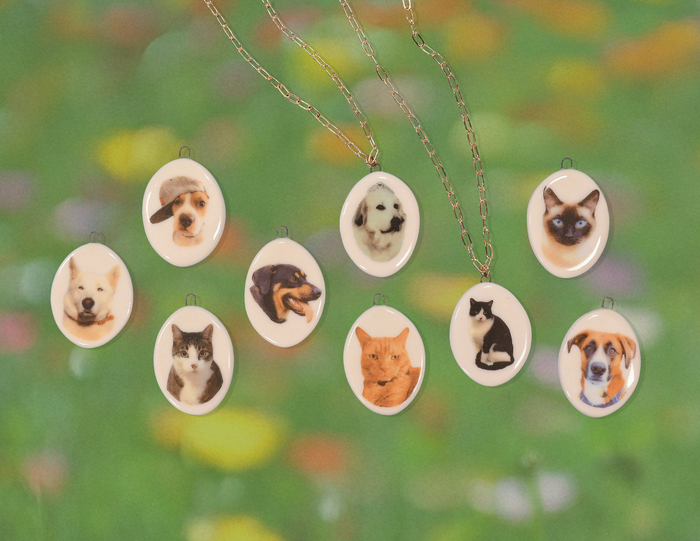 Necklaces with oval pendants featuring various dog and cat faces against a blurred green background.