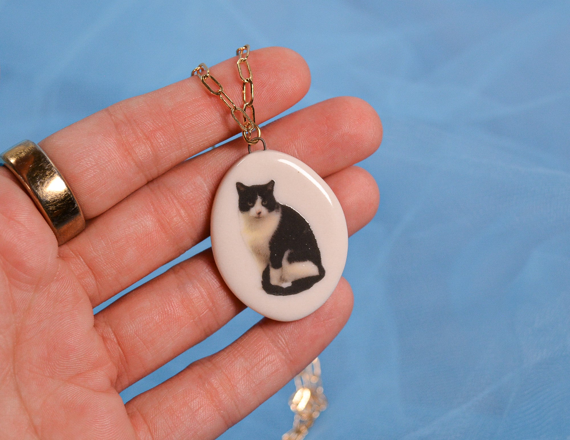 Necklace with a pendant featuring a black and white cat design held in a hand against a blue background.
