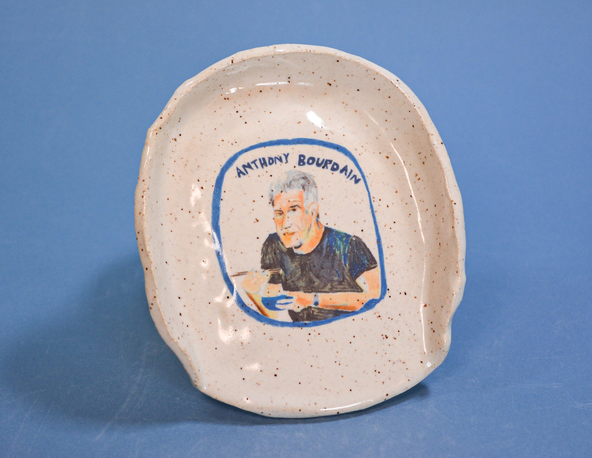 Ceramic plate with a portrait of Anthony Bourdain on a blue background