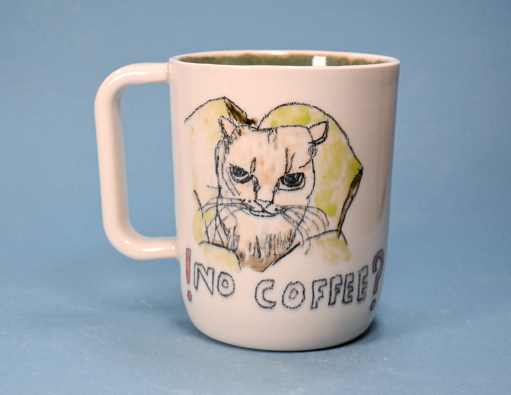 A white ceramic coffee mug featuring a hand-drawn illustration of an angry cat inside a yellow hoodie and the text '! NO COFFEE ?', set against a solid blue background.