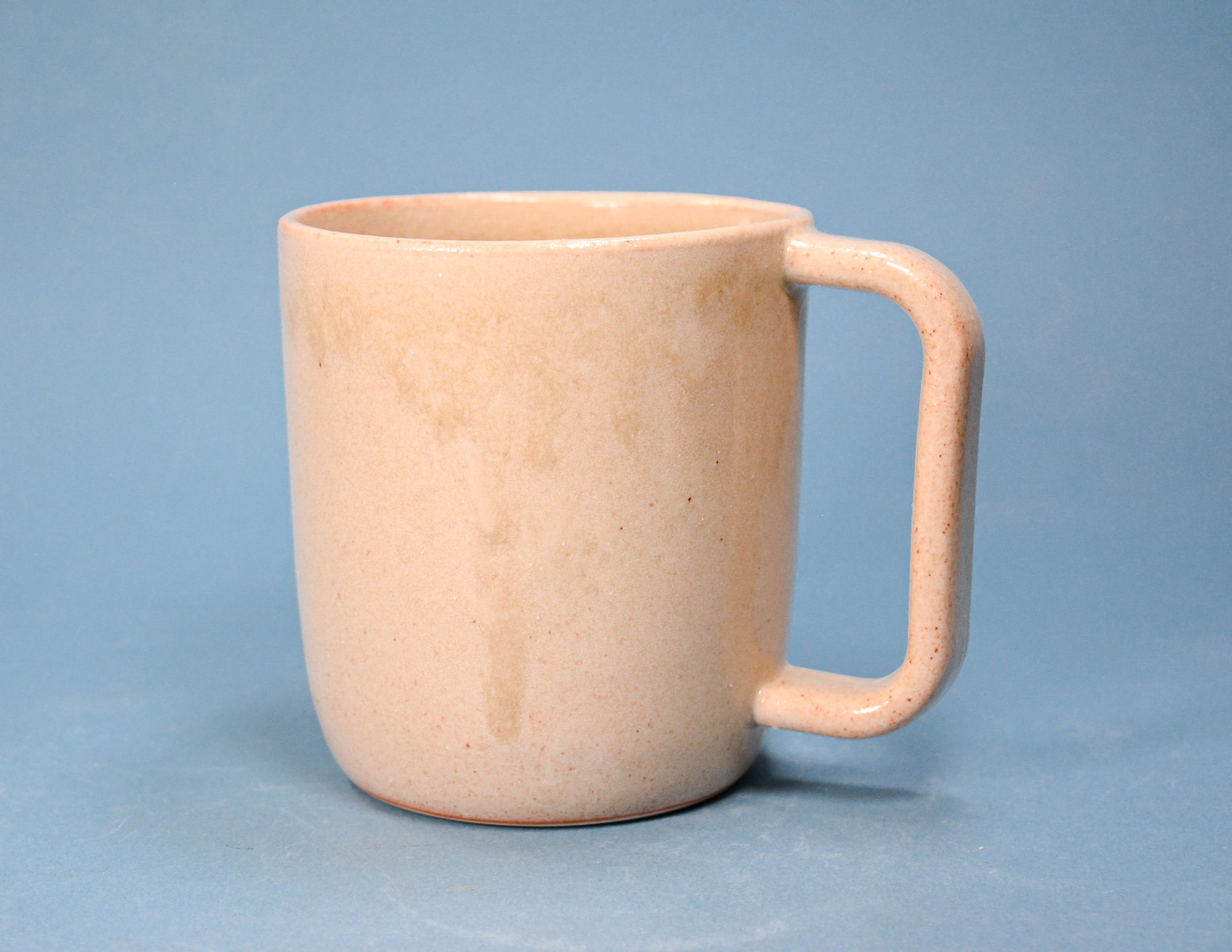 A speckled light peach ceramic mug with a rounded body and a thick integrated handle, set against a solid blue background.