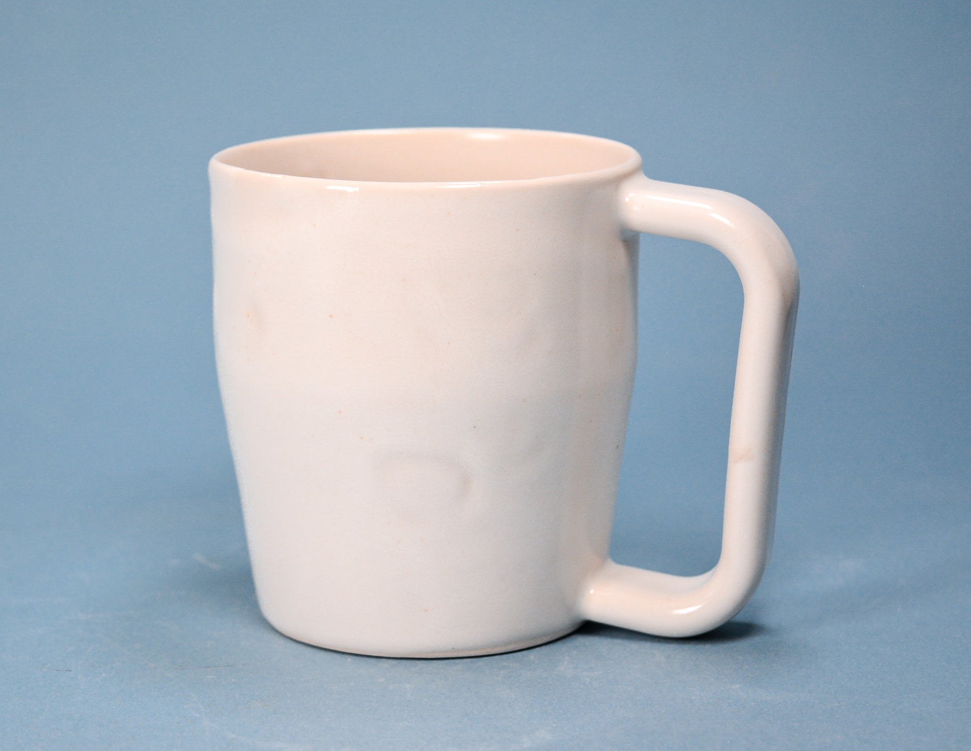 A white ceramic mug with a thick, integrated handle, shown against a solid blue background.
