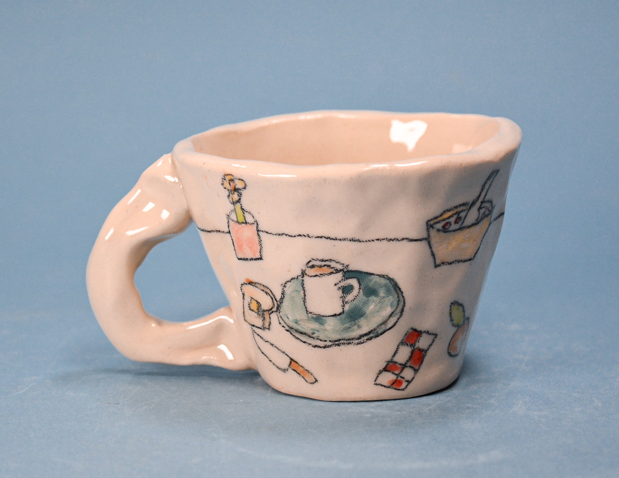 A small ceramic coffee mug with a handle, decorated with hand-painted whimsical illustrations of a coffee cup on a saucer, a bottle, and other objects, set against a solid blue background.