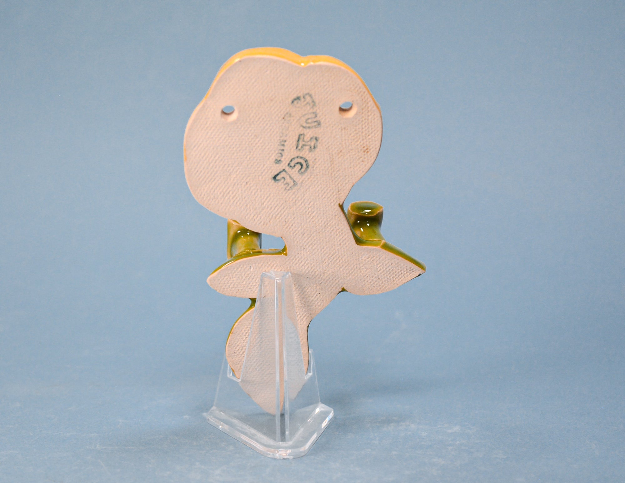 A small beige textured bird-shaped accessory with gold-toned edges and a clear stand, photographed against a soft light blue background.