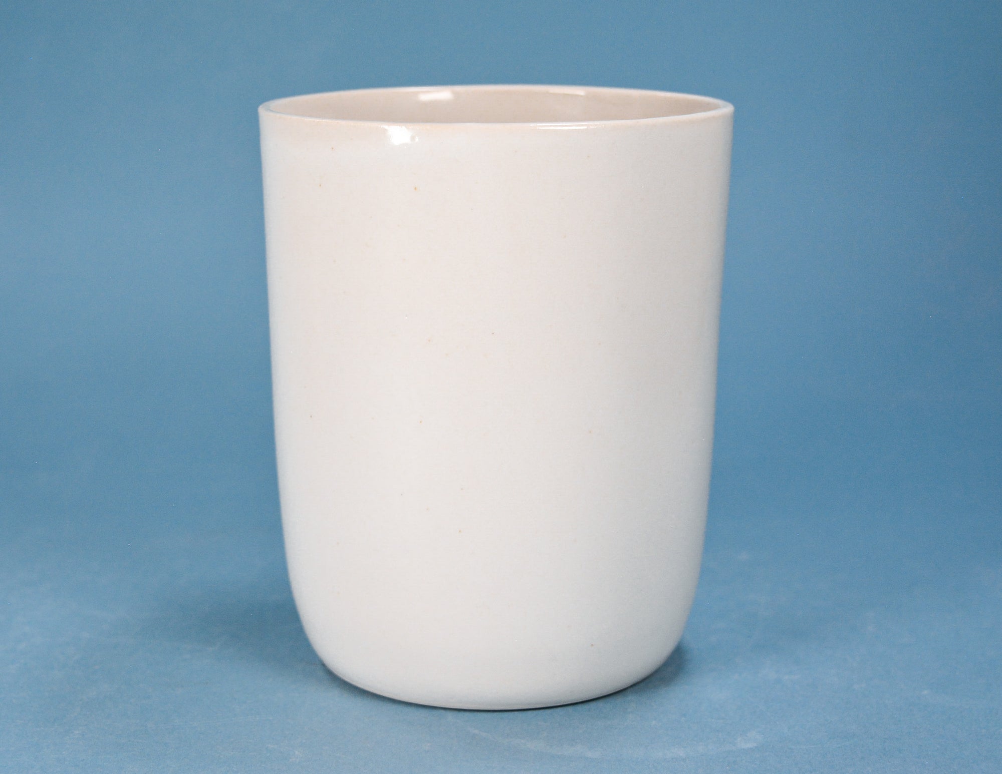 A plain white ceramic cup or tumbler with a smooth, matte finish, shown against a solid blue background.