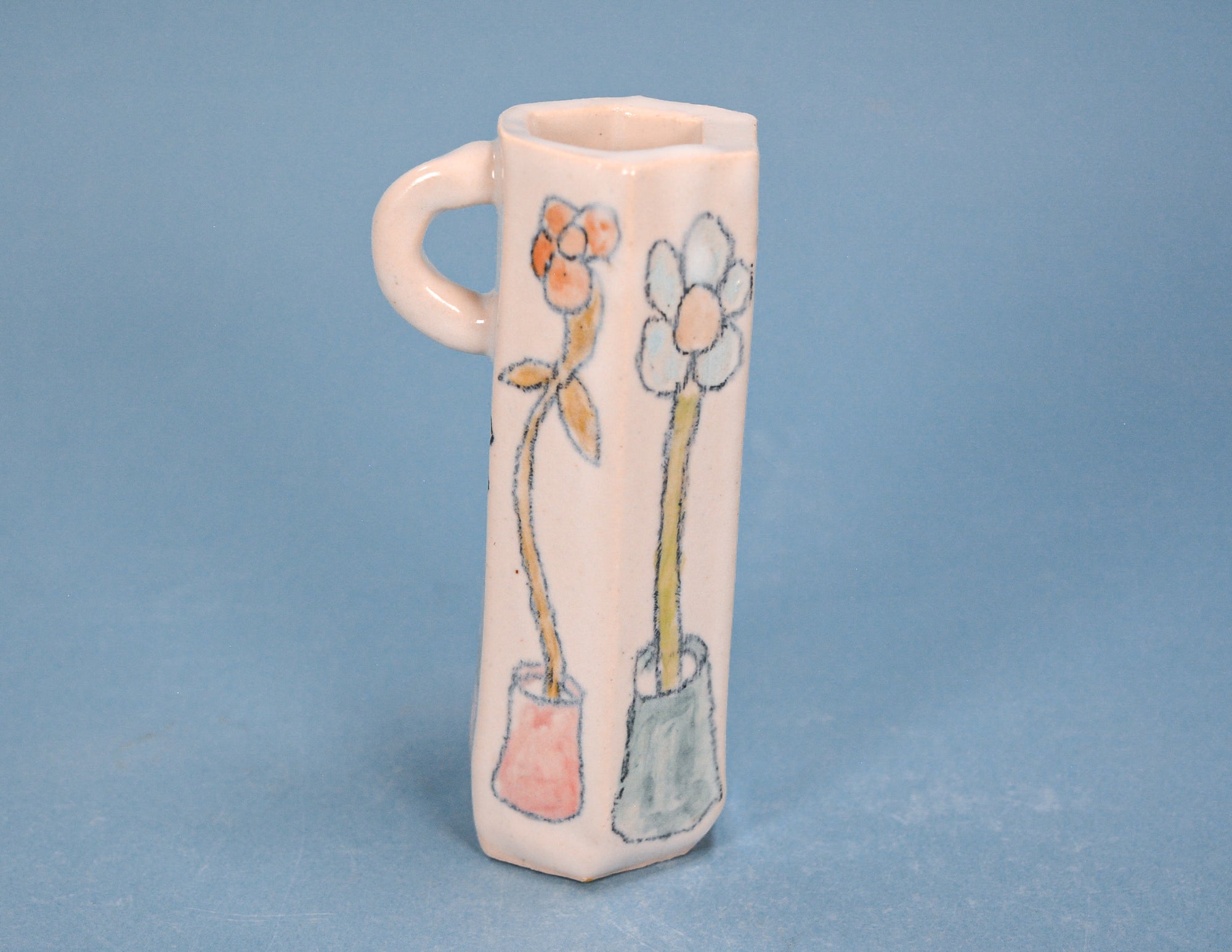 A small ceramic flower pot with a handle, featuring hand-painted flowers in pink, orange, white, and yellow on a light blue background.