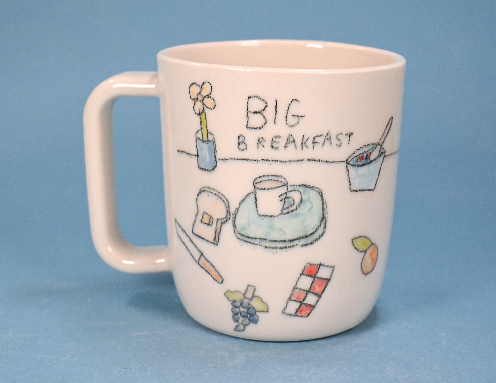 A white ceramic coffee mug with a handle, decorated with a hand-drawn style breakfast illustration and the text 'BIG BREAKFAST' on a blue background.