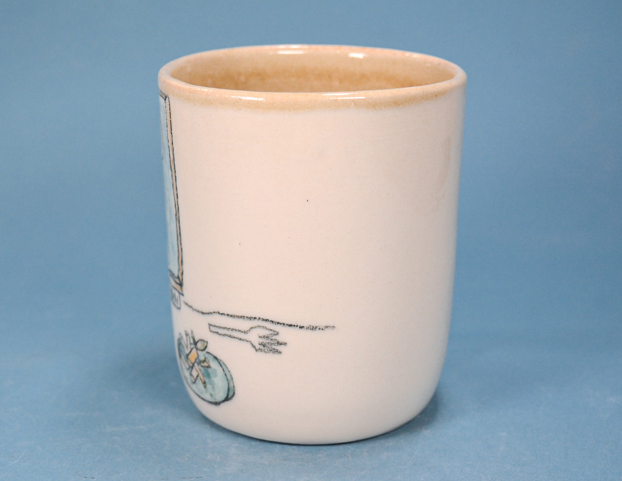 A small ceramic cup with a cream-colored exterior and a light brown glazed interior, featuring a partial hand-painted illustration in black and muted blue on the side, set against a solid blue background.