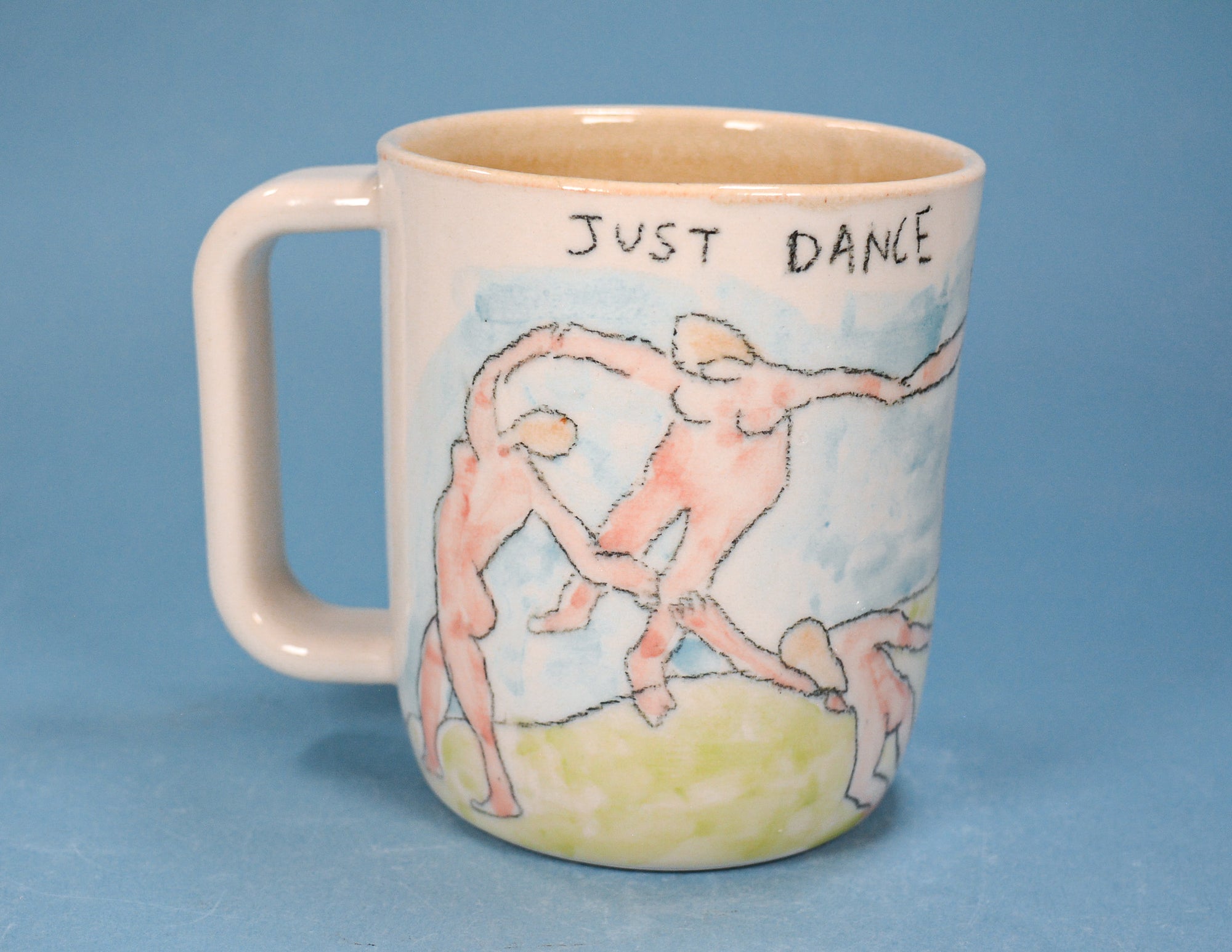 A ceramic mug with a handle, featuring a hand-painted illustration of dancing figures and the text 'JUST DANCE' on a light blue background.