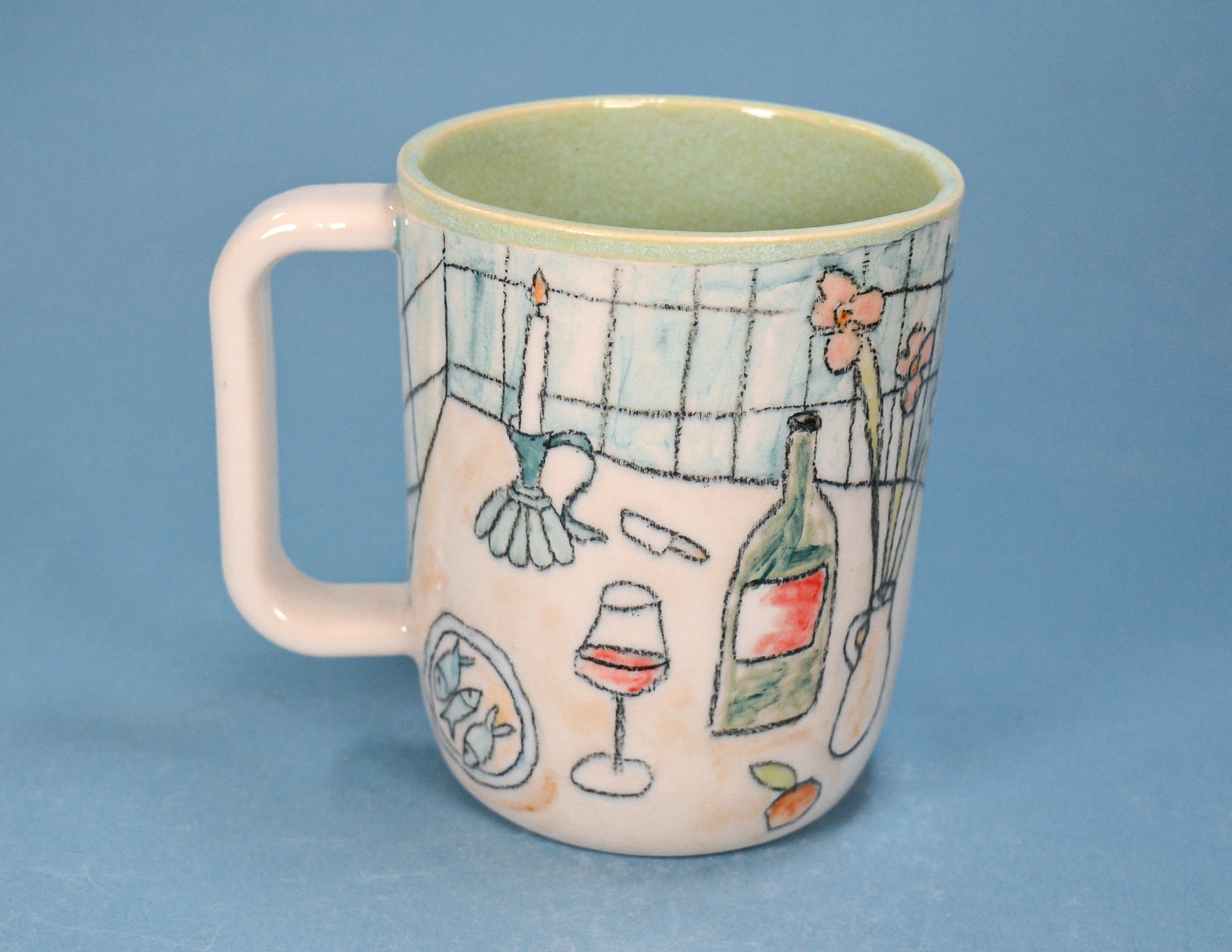 A ceramic mug with a light pink handle and exterior decorated with hand-drawn illustrations of a candle, wine glass, wine bottle, flowers, and a tiled wall, set against a solid blue background.