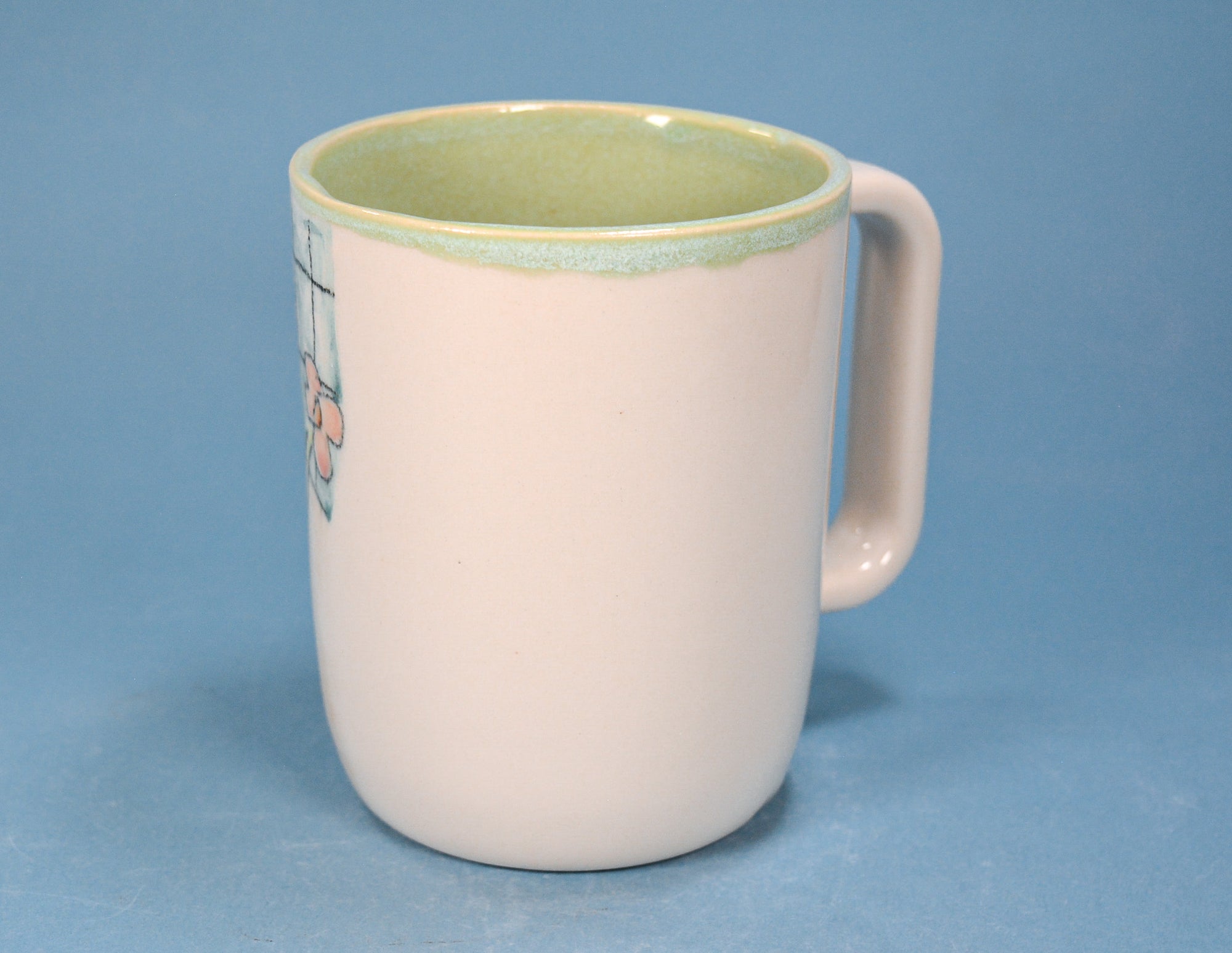 A ceramic mug with a pale pink exterior, a light green glazed interior, and a matching green rim, shown against a solid blue background.