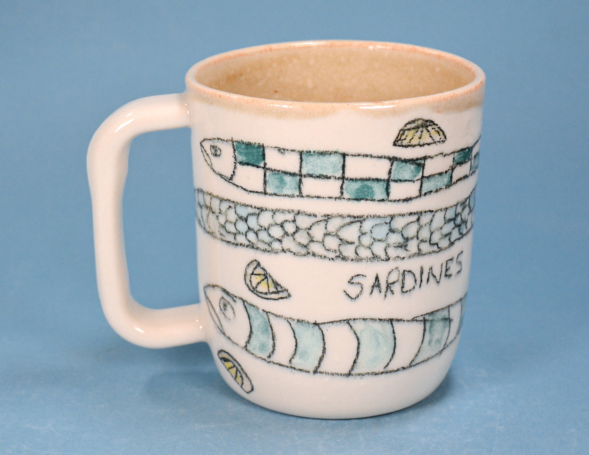 A ceramic mug with a handle, decorated with painted sardine illustrations, lemon slices, and the word 'SARDINES' in black lettering, set against a solid blue background.