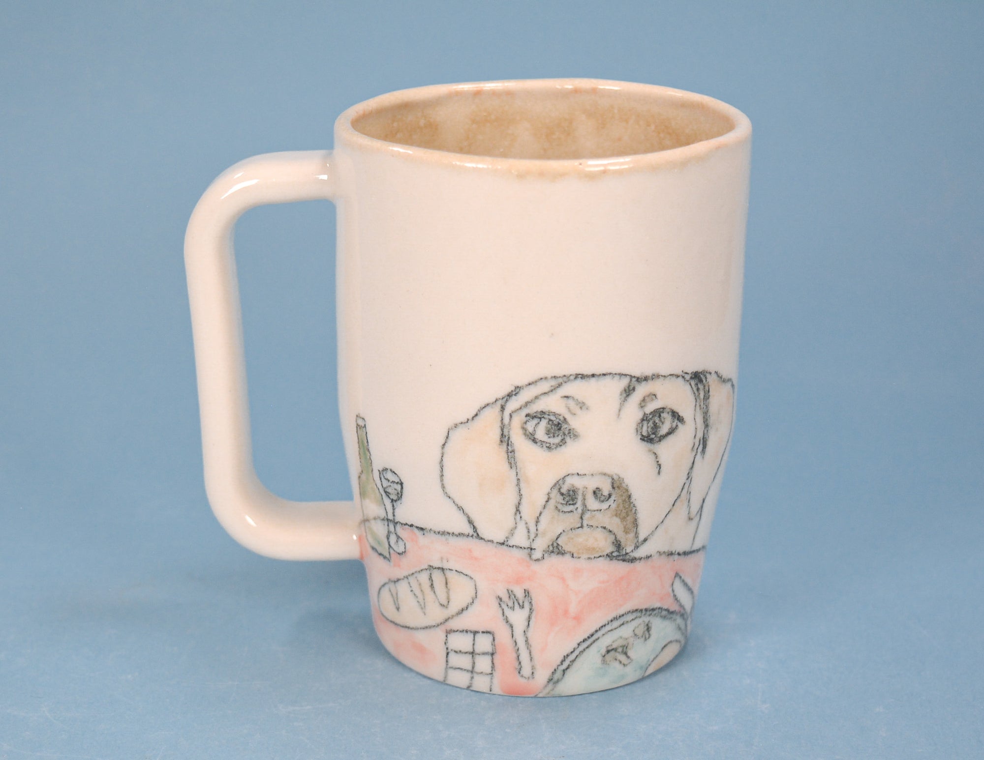 A cream-colored ceramic mug with a handle, featuring a hand-drawn sketch of a dog's face and a pink table setting on the lower half, set against a solid blue background.