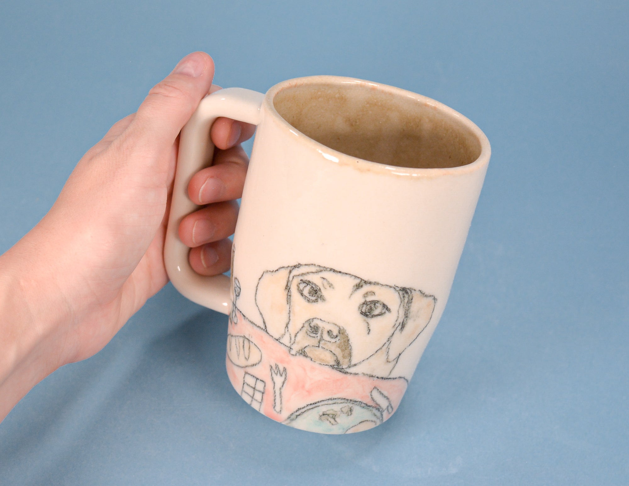 A hand holding a cream-colored ceramic mug with a hand-drawn illustration of a dog on the side, set against a solid blue background.