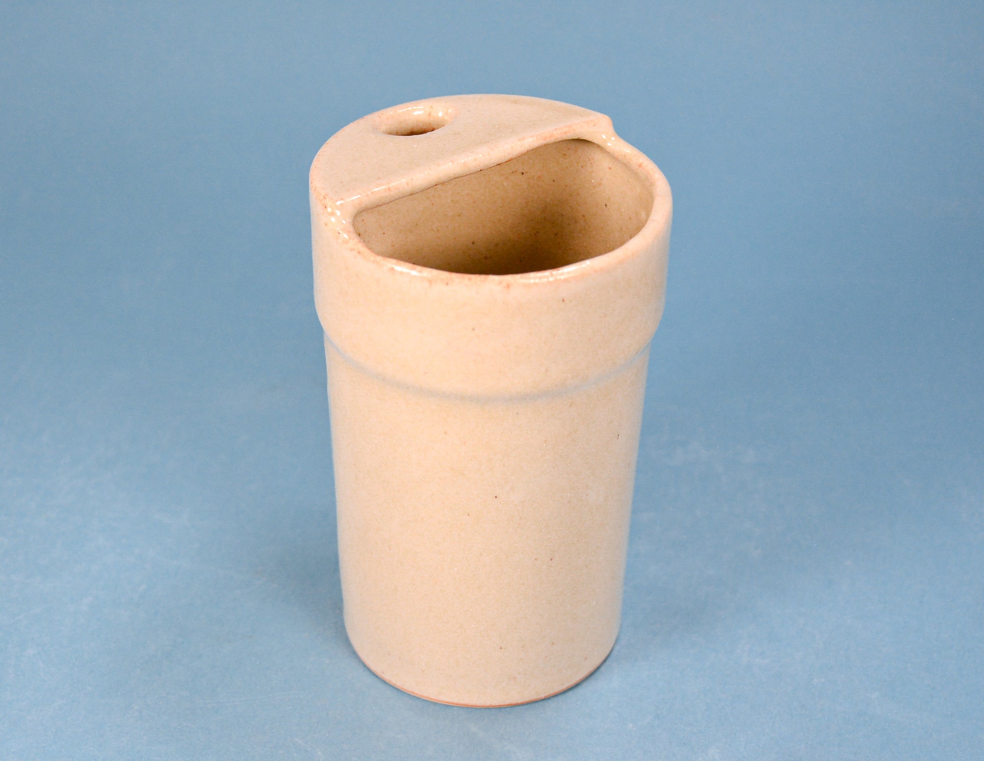 A small cylindrical ceramic cup or candle holder with a small hole in the lid, shown on a solid blue background.