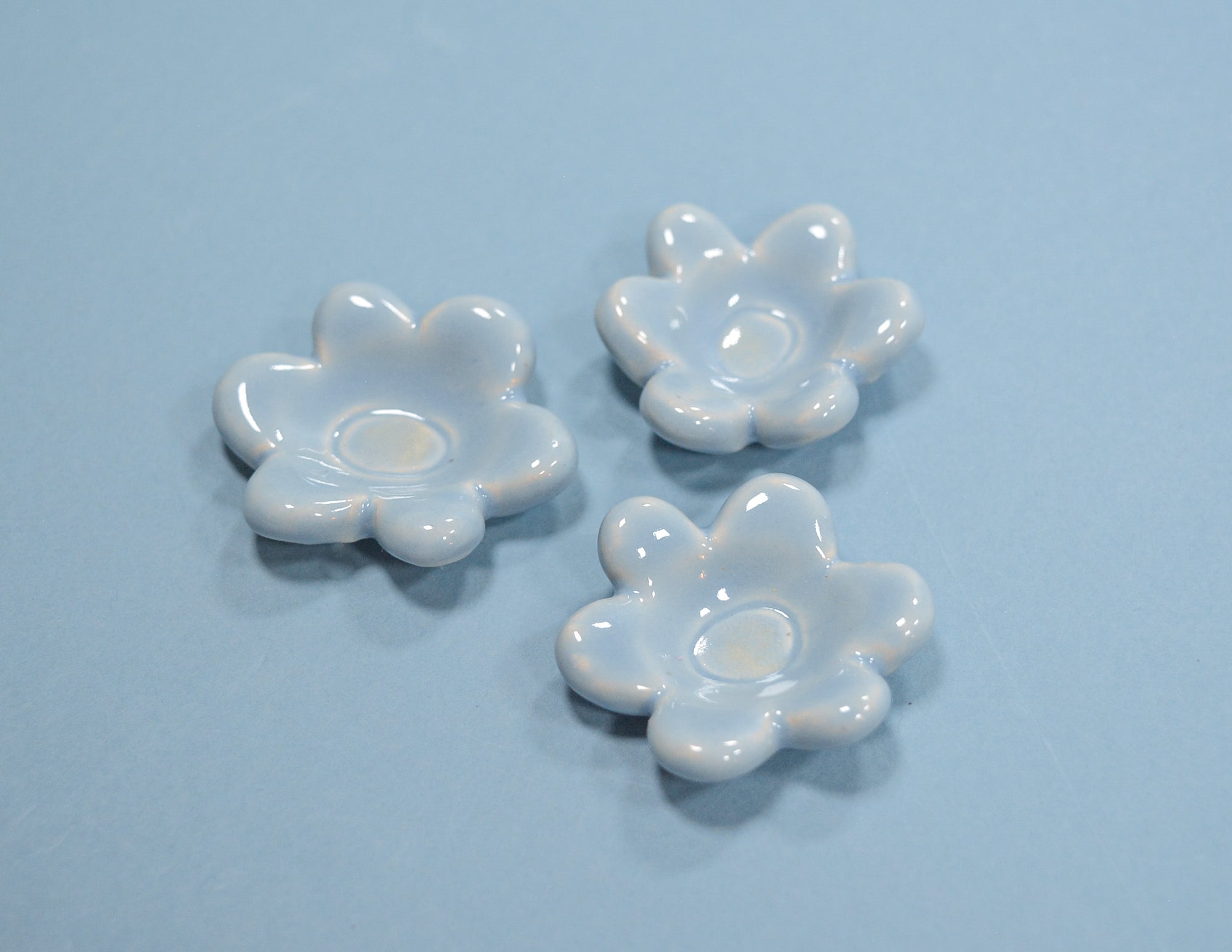 Three small glossy white flower-shaped dish holders arranged on a light blue background.