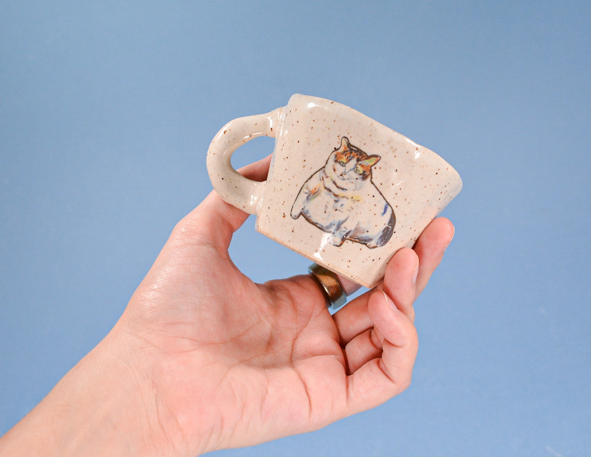 Hand holding a small ceramic mug with a dog design against a blue background