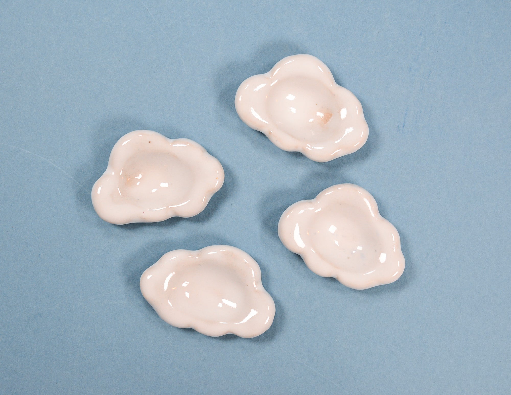 Four small glossy cloud-shaped worry stones in a pale pink color, arranged on a solid light blue background.