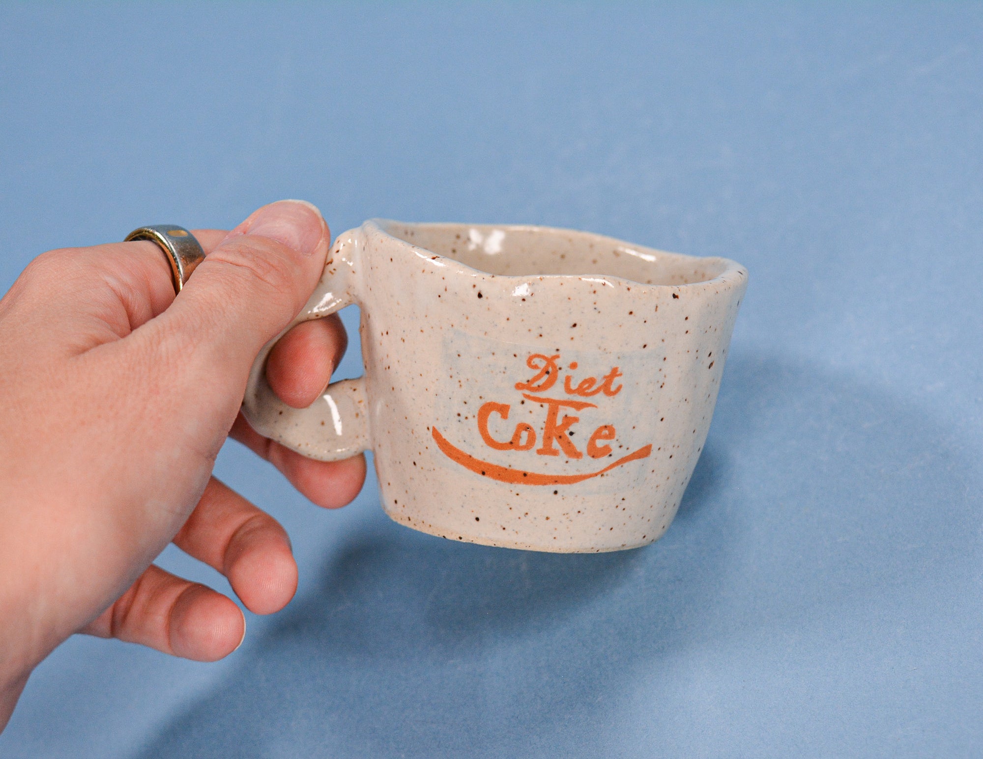 Hand holding a ceramic mug with 'Diet Coke' text against a blue background