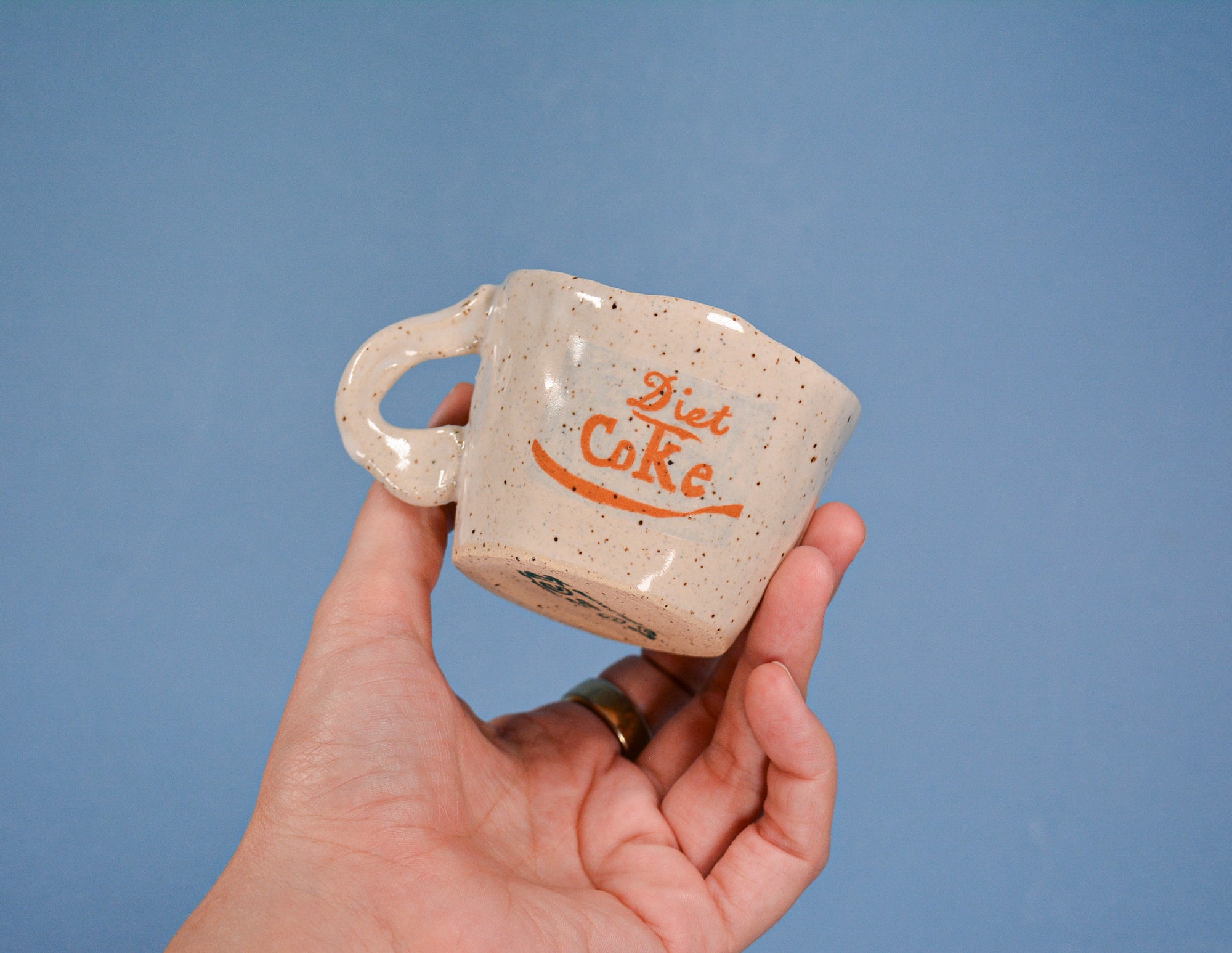 Hand holding a ceramic mug with 'Diet Coke' branding against a blue background