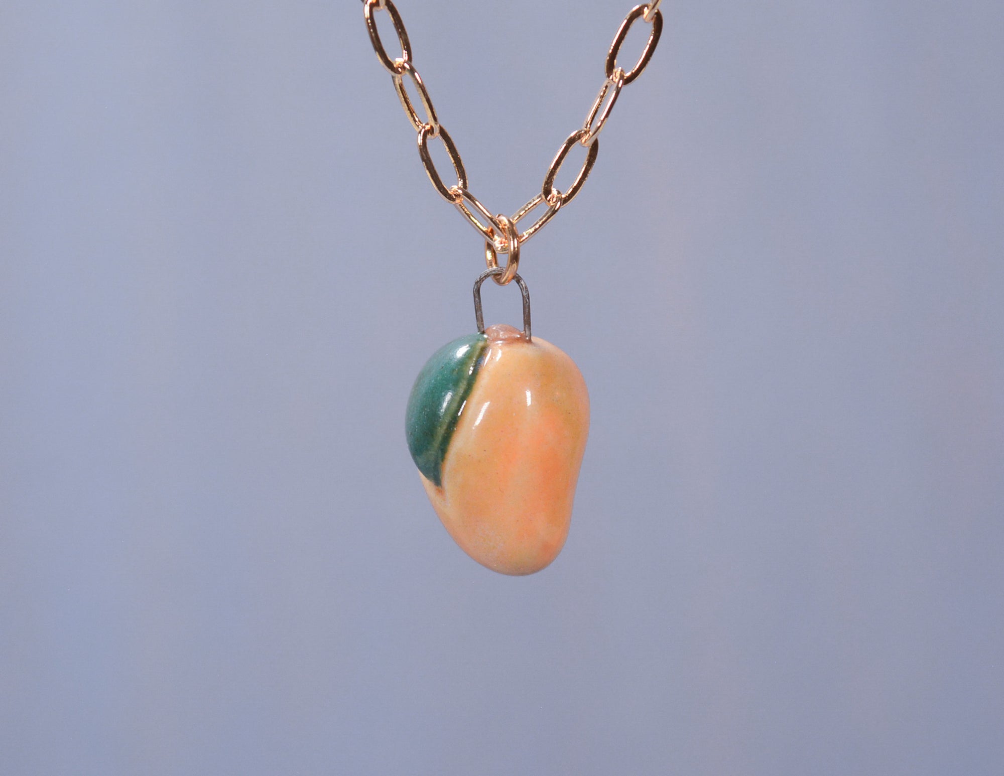 A hand sculpted ceramic pendant necklace with a gold-plated chain, featuring colors resembling a mango.